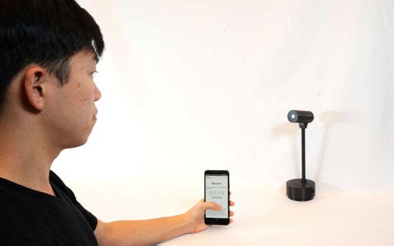 Person holding smartphone while looking at Beacon device